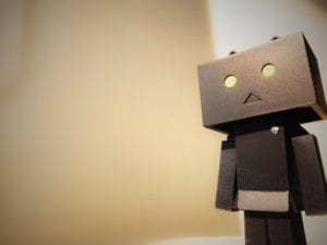 Photo of gray robot figure frowning and looking sad with light brown background