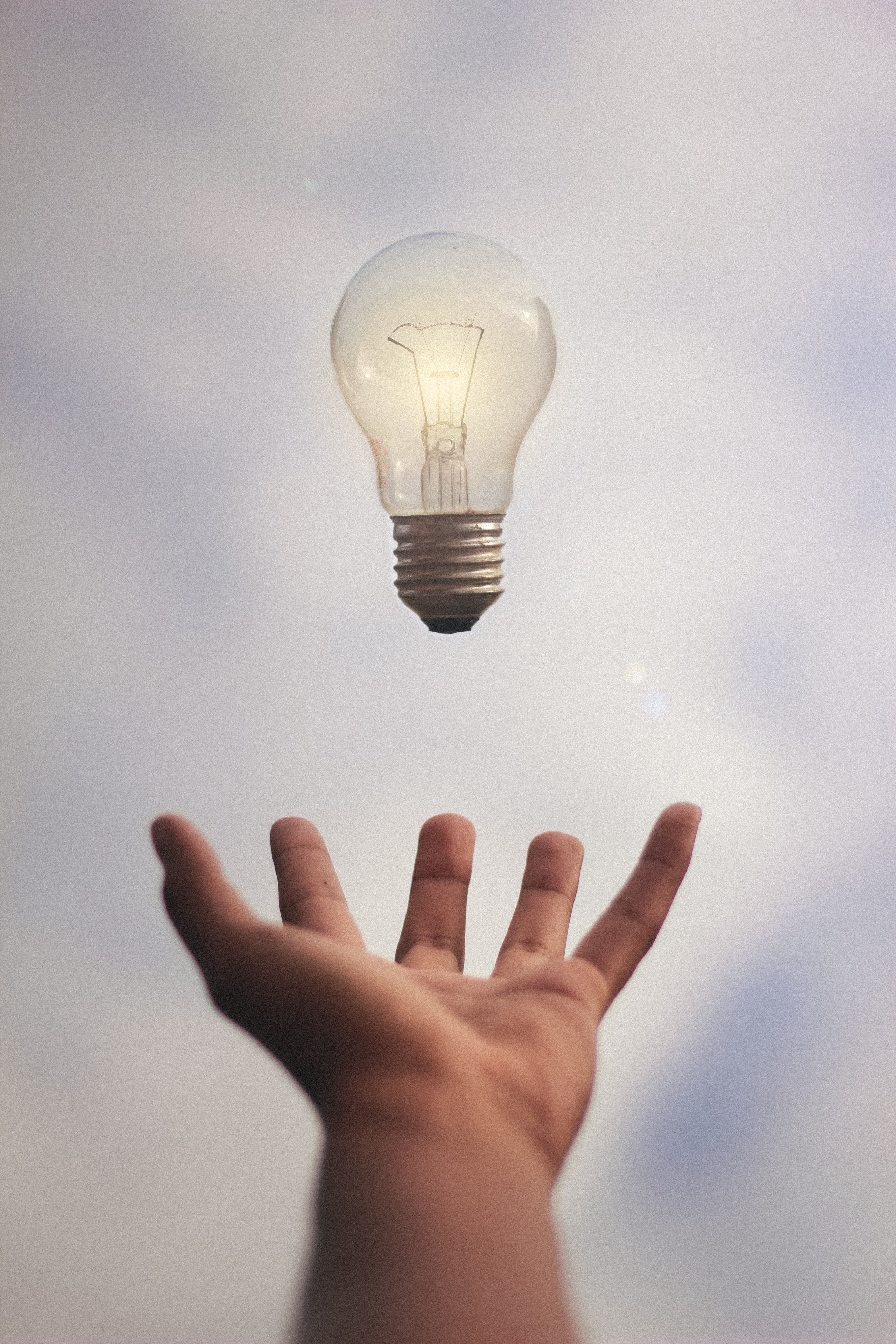 A light bulb with a hand underneath, as if suspending the bulb in midair