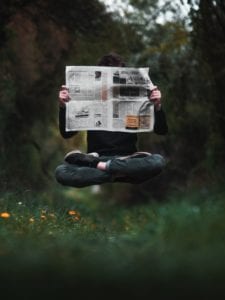 A person reading the paper while floating in the air in a meadow