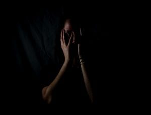 a woman holding her face in a dark room. She looks stressed out.